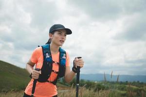 Young women active trail running across a meadow on a grassy trail high in the mountains in the afternoon with trekking pole photo