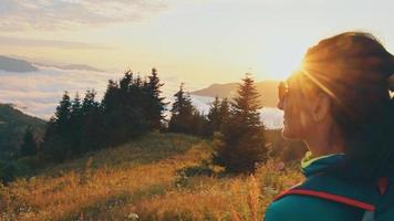 Lonely happy woman portrait watch sunrise. Carefree tourist woman looking at sun enjoying landscape. Girl traveler on top of mountain in rays of sunset. Hiker is enjoying nature video