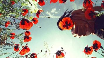 Young dreamy girl hold poppy flower low angle surrounded poppy field and blue sky background.Well being and Feeling free and happy, optimistic nature shot video