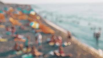 Zoom in copy space blurry background tourist on crowded summer beach by sea relax. Intentional blur effect filter video