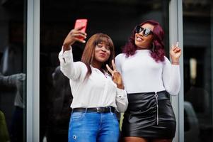 Two female friends african american models posed outdoor with mobile phone at hand. photo