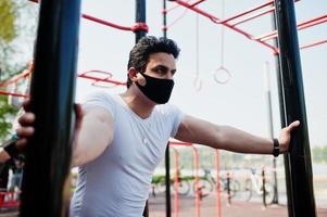 Portrait sports arabian man in black medical face mask doing workout exercises in outdoor gym place during coronavirus quarantine. photo