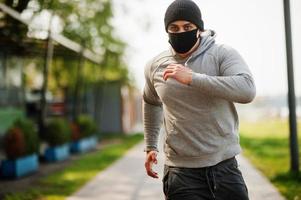 retrato deportivo hombre árabe con mascarilla médica negra correr al aire libre durante la cuarentena del coronavirus. foto