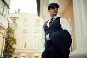 Portrait of retro 1920s english arabian business man wearing dark suit, tie and flat cap. photo