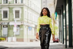 retrato de una joven y bella modelo afroamericana, vestida con top verde y pantalones negros brillantes de aspecto húmedo. foto