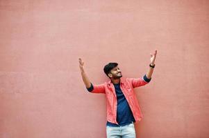 Portrait of young stylish indian man model isolated on pink wall background. Hands to air. photo