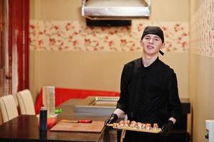 Professional chef wear in black with sushi and rolls in a restaurant of japanese traditional food. photo