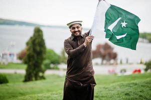 pakistaní pathan el hombre usa ropa tradicional y sostiene la bandera de pakistán. foto