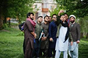 grupo de hombres paquistaníes vestidos con ropa tradicional salwar kameez o kurta haciendo selfie en el teléfono móvil. foto