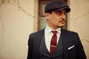 Portrait of retro 1920s english arabian business man wearing dark suit, tie and flat cap. photo