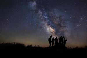 Landscape with milky way, Night sky with stars and silhouette of happy people standing on the mountain, Long exposure photograph, with grain photo