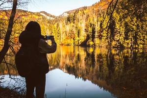 Close up cinematic back view caucasian woman hiker stand by lake take photo of scenic autumn nature outdoors in sunny day outdoors . Famous travel destination in Georgia