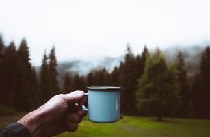 Blue cup in hands with forest background. Cinematic travel inspirational background photo