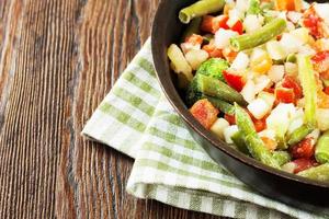 Mixture of frozen vegetables on brown wooden background photo