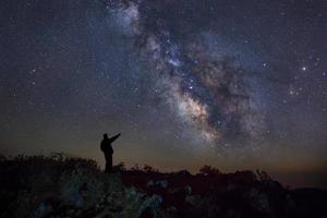 un hombre está de pie junto a la galaxia de la vía láctea apuntando a una estrella brillante, fotografía de larga exposición, con grano foto