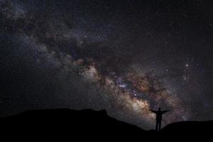 Landscape with milky way, Night sky with stars and silhouette of a standing happy man on the mountain, Long exposure photograph, with grain photo