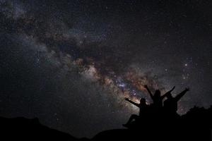 paisaje con vía láctea, cielo nocturno con estrellas y silueta de personas sentadas en la montaña, fotografía de larga exposición, con grano foto