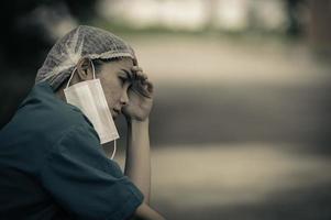 una enfermera asiática cansada y deprimida usa una máscara facial uniforme azul sentada en el piso del hospital, una joven doctora estresada por el trabajo duro foto