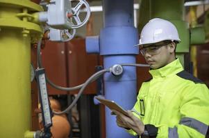 Asian engineer wearing glasses working in the boiler room,maintenance checking technical data of heating system equipment,Thailand people photo