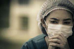 Tired depressed female asian scrub nurse wears face mask blue uniform sits on hospital floor,Young woman doctor stressed from hard work photo