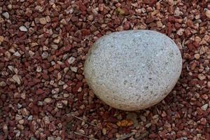 Round stone lies on decorative pebbles of red color. photo