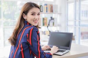 Asian confident woman is resting her hand on the keyboard of laptop and turn back her face with smiling in a working room at home. photo