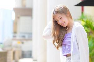 hermosa mujer asiática con cabello largo bronce en camisola morada y manga blanca se encuentra en la calle como fondo. foto