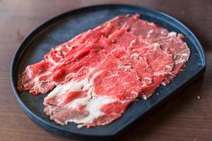 Se sirvió carne de res fresca cortada en rodajas para el restaurante sukiyaki y shabu o yakiniku que se puso en un plato negro. foto