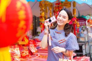 mujer asiática con vestido chino gris sostiene una cámara rosa en la mano y sonríe entre el tema de la ciudad china. foto