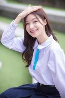 Beautiful Asian high school student girl in the school uniform with braces on her teeth sitting and smiles confidently while she looks at the camera happily with the building in the background. photo