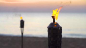 antorcha de bambú con luz de gas de primer plano que quema una playa decorativa durante la puesta de sol.
