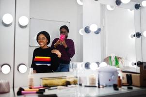 mujer afroamericana aplicando maquillaje por maquillador en el salón de belleza. artista hace una foto en el teléfono móvil de su trabajo.