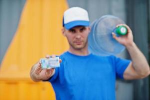 Delivery man carrying water bottle on shoulder and show business card. photo