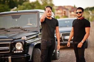 dos hermanos asiáticos se visten de negro y posan cerca de los autos todoterreno. foto