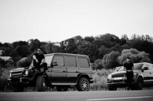 Two asian brothers man wear on all black posed near suv cars. photo