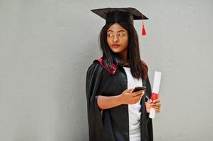 joven estudiante afroamericana con diploma y teléfono móvil posa al aire libre. foto