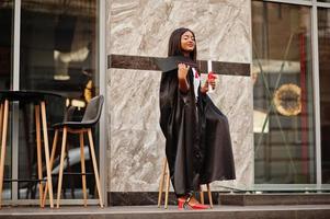 joven estudiante afroamericana con diploma posa al aire libre. foto