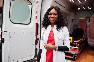 African american female paramedic standing in front of ambulance car. photo