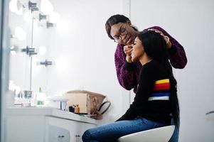 mujer afroamericana aplicando maquillaje por maquillador en el salón de belleza. foto