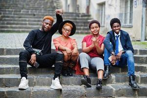 Four african friends having fun outdoors. Two black girls with guys sit on stairs of an old city. photo