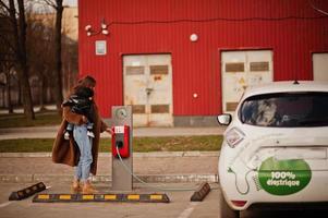 joven madre con niño cargando electro coche en la gasolinera eléctrica. foto