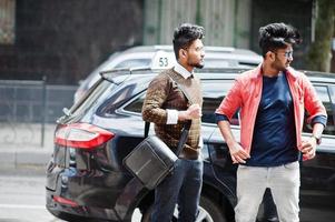 Two young stylish indian man frieds model posing in street against black taxi car. photo