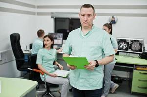 Medical theme .Portrait of male doctor with clipboard against group of doctors meeting in the mri office at diagnostic center in hospital. photo