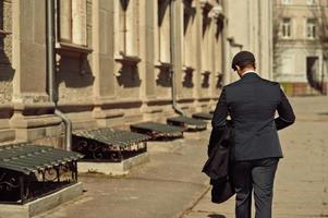 Back of retro 1920s english arabian business man wearing dark suit, tie and flat cap. photo