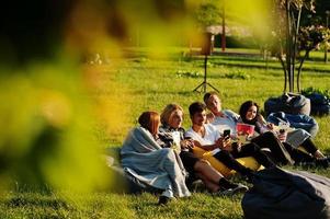 Young multi ethnic group of people watching movie at poof in open air cinema. photo