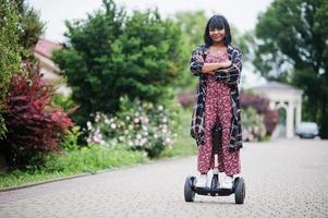 hermosa mujer afroamericana usando segway o hoverboard. chica negra en scooter eléctrico autoequilibrado de doble rueda. foto