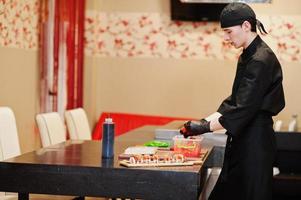 chef profesional vestido de negro haciendo sushi y rollos en la cocina de un restaurante de comida tradicional japonesa. foto