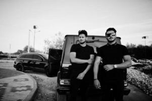 Two asian brothers man wear on all black posed near suv cars. photo