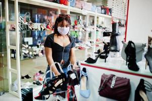 mujer afroamericana con mascarilla médica protectora para la cara para protegerse de enfermedades virales en la tienda de zapatos durante la pandemia del coronavirus. foto