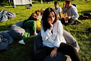 Young multi ethnic group of people watching movie at poof in open air cinema. Close up portrait of funny girl. photo